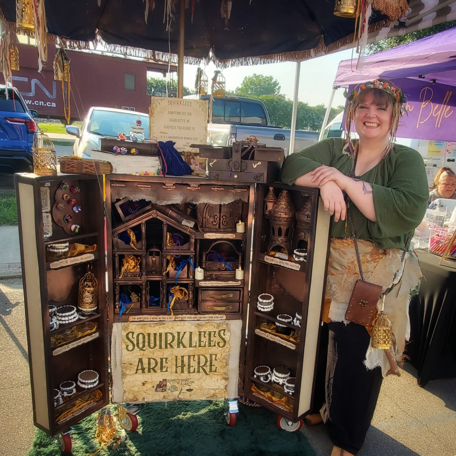 Magical female leaning on a wooden Squirklee adoption cabinet case at an outdoor event.