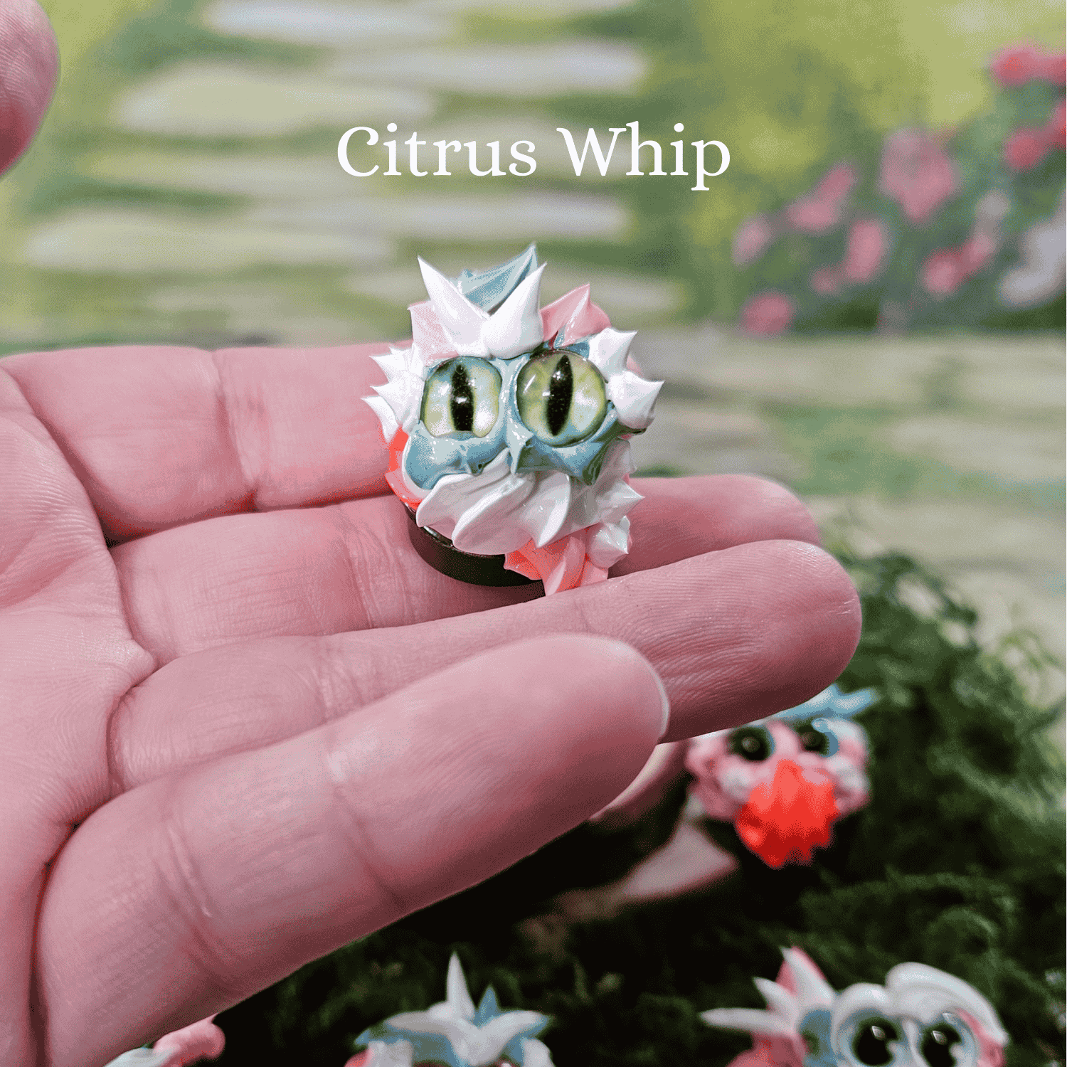 Small, colorful frosting creature held in a hand with a garden background