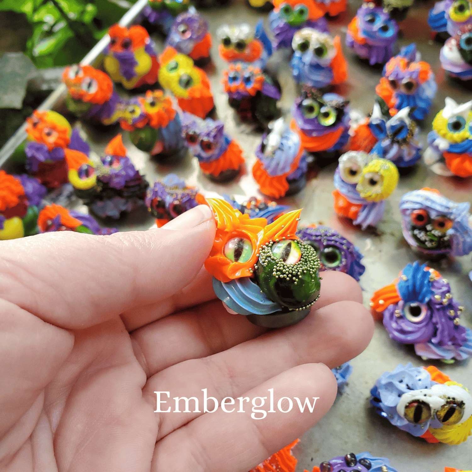 Colorful miniature frosting creatures held by a hand with 'Emberglow' branding.