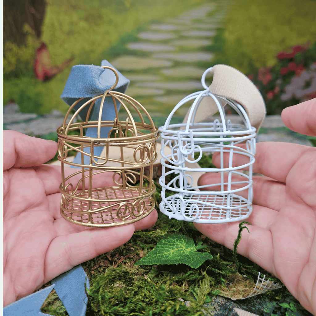 Two miniature wire cages, one gold and one white, held in hands with a garden background.