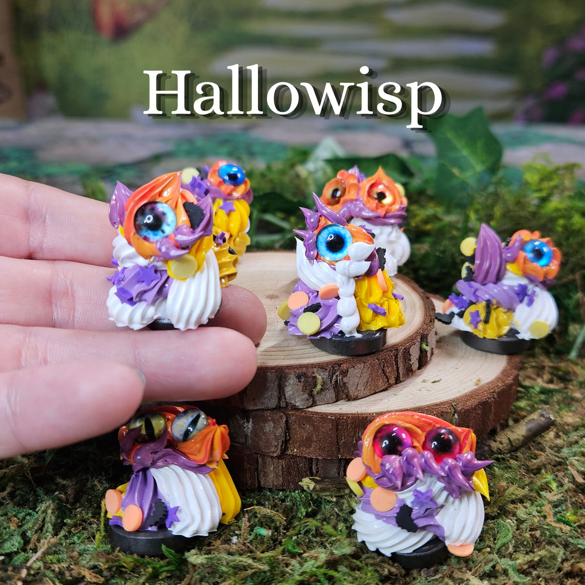 Hand holding a small colorful frosting figurine, with several matching owl figurines displayed on mossy ground and stacked wood slices. The word 'Hallowisp' appears at the top.