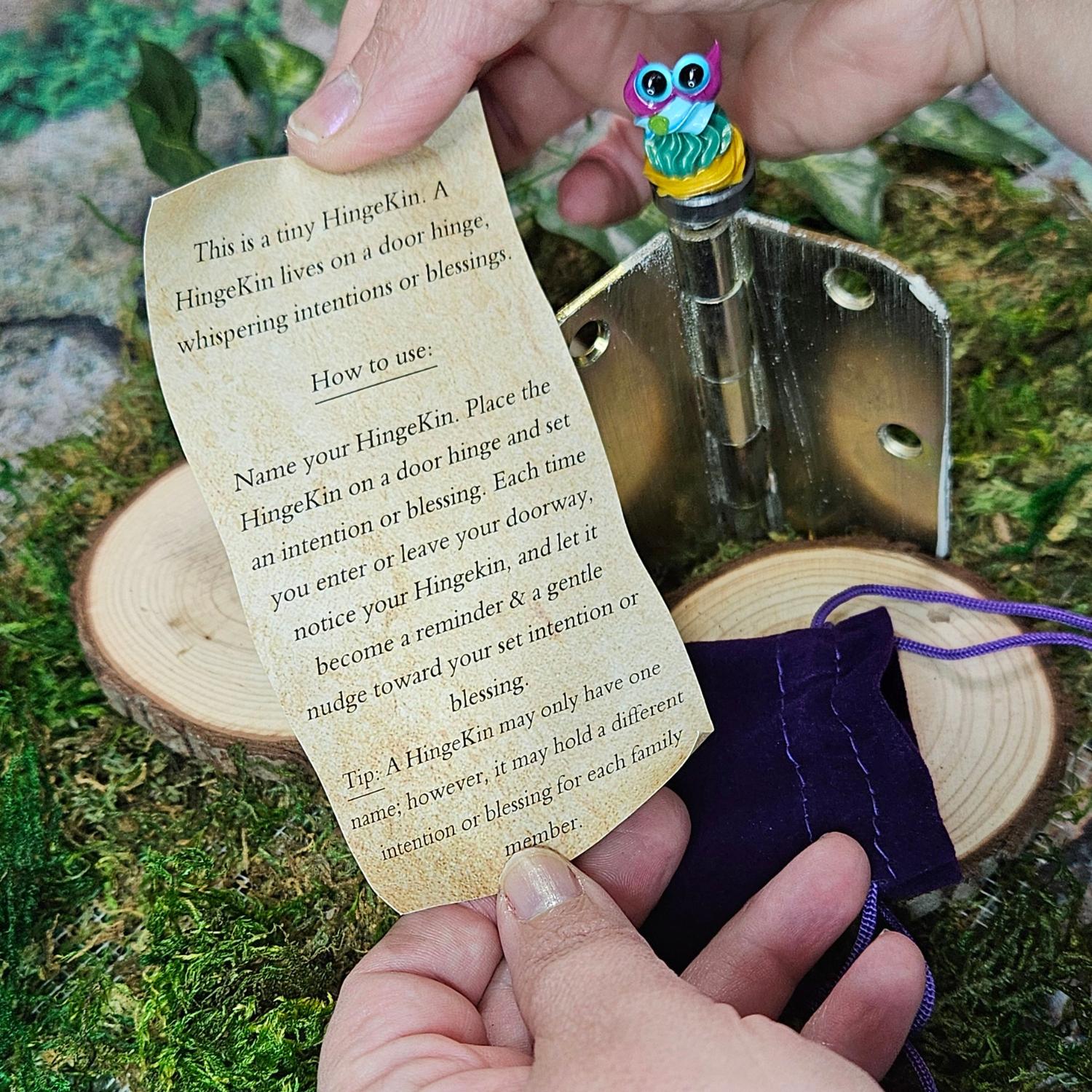 super tiny frosting style creature on magnet sitting on a door hinge to carry intentions or blessings, posed with a hand, velvet bag and open scroll with instructions