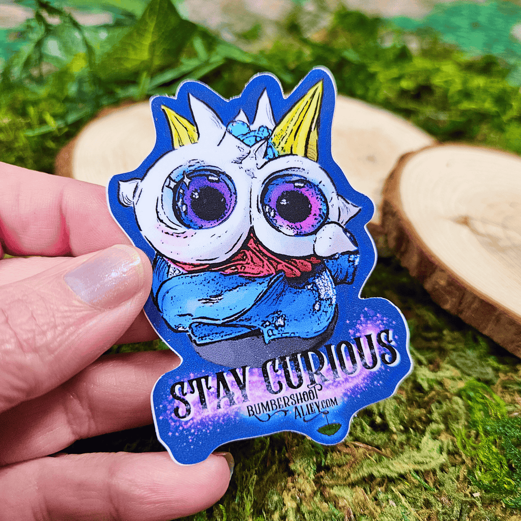 Hand holding a colorful sticker with a frosting creature design on a natural background