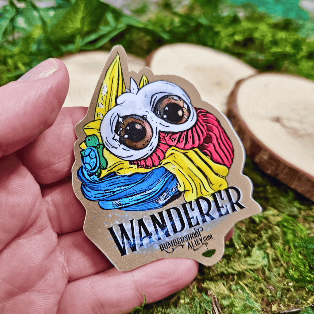 Colorful sticker of a frosting creature with 'Wanderer' text held in a hand on a natural background