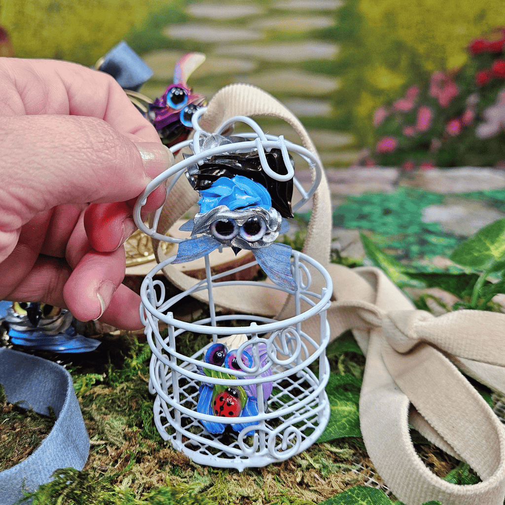 Small blue frosting creature in a white cage held by a hand with a garden background