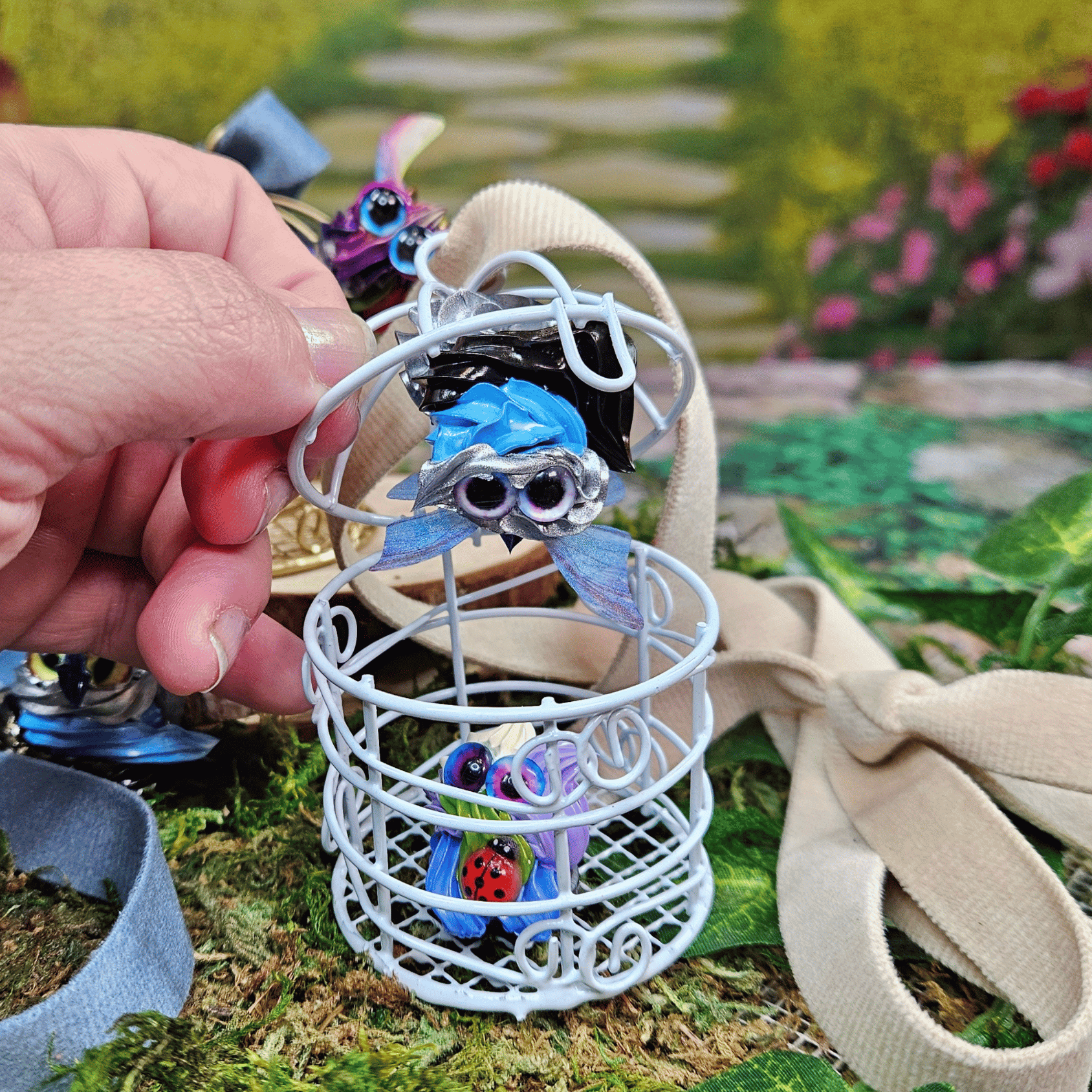 Small blue frosting creature in a white cage held by a hand with a garden background